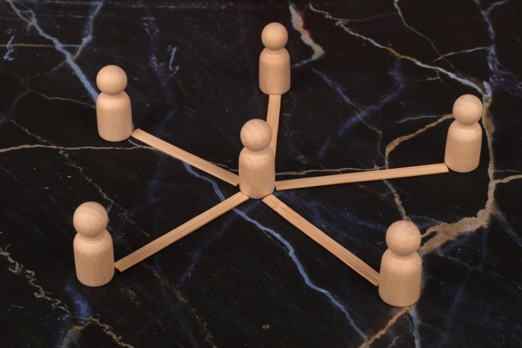 Wooden figures arranged in a network pattern on a marble surface, symbolizing connection or teamwork.